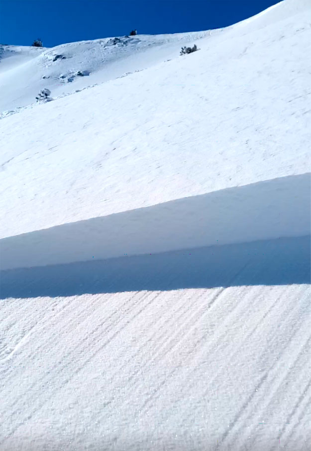 En primer plano la cicatriz de la placa de viento, con los bordes más delgados y el centro más grueso. La placa se desliza sobre una superficie lisa. El manto nivoso en superficie presenta las típicas ondulaciones de nieve venteada (Imagen cedida por R. Martínez).